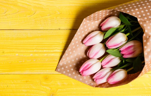 Spring is here. Happy birthday. Bouquet fresh pink tulips on yellow table background top view. Spring holiday greetings. Spring flowers for mothers day. Spring vibes. Surprise for darling copy space