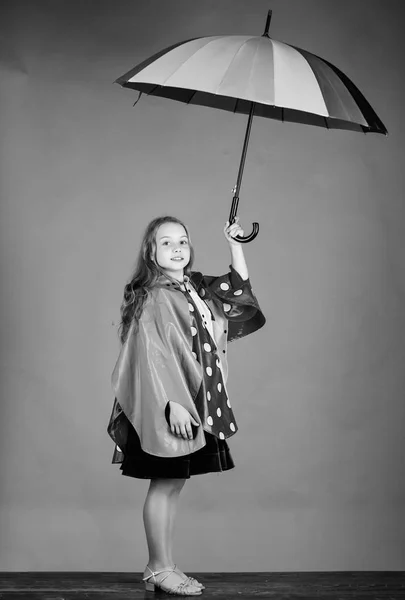 Ragazza felice tenere colorato ombrello indossare mantello impermeabile. Godetevi il tempo piovoso con indumenti adeguati. Gli accessori impermeabili rendono la giornata piovosa allegra e piacevole. Accessori impermeabili per bambini — Foto Stock
