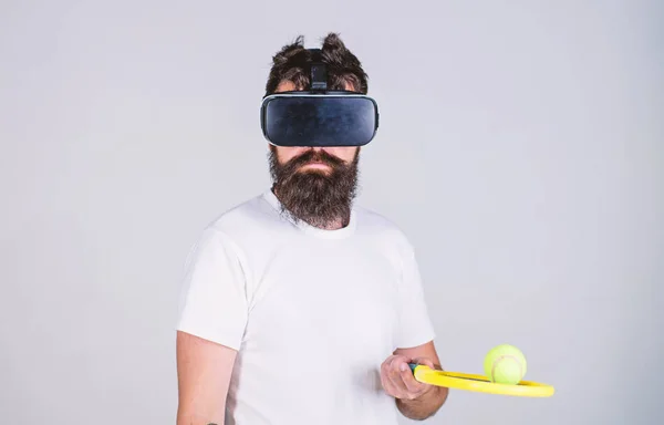 Homem com barba em óculos VR jogar tênis, fundo cinza. Hipster no rosto calmo usar tecnologia moderna para jogos esportivos. Conceito de desporto virtual. Cara com óculos VR jogar tênis com raquete e bola — Fotografia de Stock