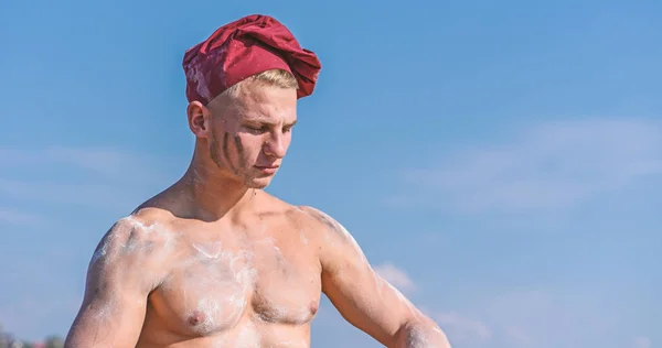 Chef en chapeau de marsala sur le ciel du visage strict sur le fond. Concept de chef sexy. Homme avec l'aspect attrayant fonctionne comme cuisinier ou boulanger, espace de copie. Homme avec torse musculaire recouvert de farine semble attrayant — Photo