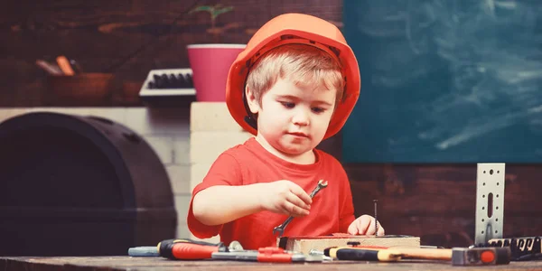 童年的概念。男孩扮演建设者或修理工, 使用工具。男孩在橙色硬帽子或头盔, 学习室背景。孩子梦想未来的建筑或建筑事业 — 图库照片