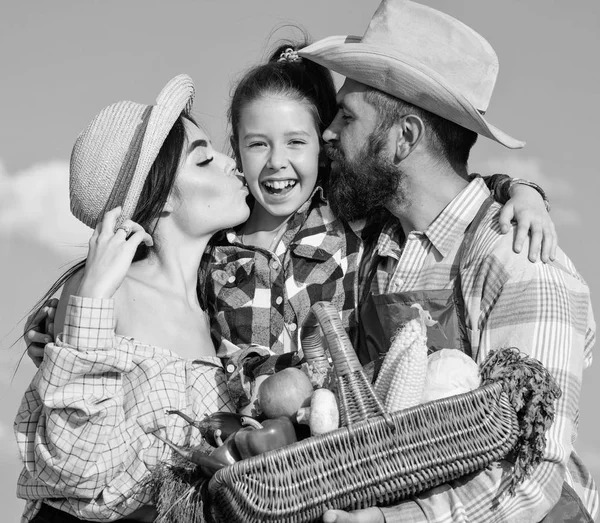 Family farmers hug kiss kid hold basket fall harvest. Family gardener basket harvest blue sky background. Family gardening. Family farm concept. Parents and daughter farmers celebrate harvest holiday