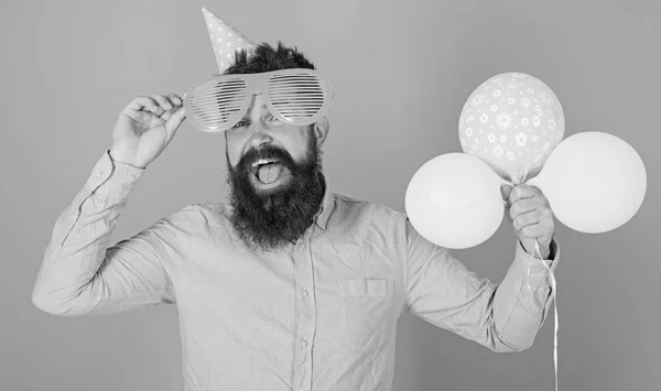 Hipster em óculos gigantes celebra o aniversário. Partido atribui conceito. Homem com barba no rosto feliz segurar balões de ar, fundo azul claro. Cara em chapéu de festa com balões de ar celebra — Fotografia de Stock