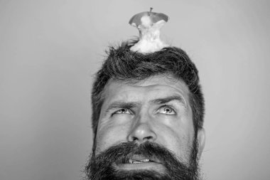 Adam yakışıklı hipster uzun sakal neredeyse kafasına elma güdük hedef olarak yem. Diyet hedefi. Canlı hedef kavramı. Hipster mutsuz yüz ile baş mavi arka plan, elma güdük hedefe yakın çekim