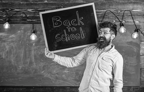 High school concept. Man with beard and mustache on cheerful face welcomes students, chalkboard on background. Teacher in eyeglasses holds blackboard with title back to school — Stock Photo, Image