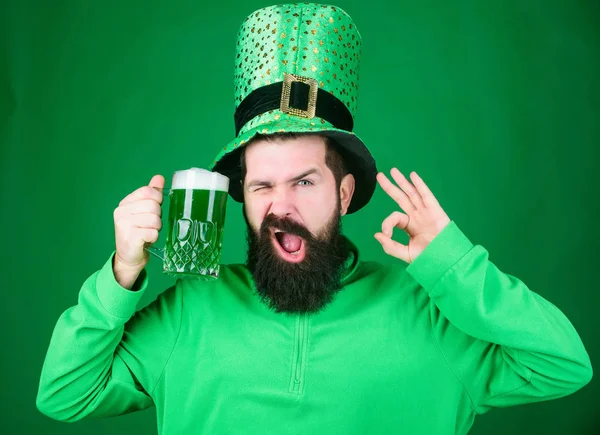 The best beer is irish. Bearded man toasting to saint patricks day. Hipster in leprechaun hat holding beer mug. Celebrating saint patricks day in bar. Irish man gesturing ok sign to green beer