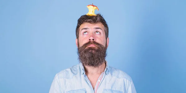 Live target concept. Man handsome hipster long beard almost eaten apple stump on head as target. Weight loss goal. Hipster surprised face with apple stump target on head blue background, copy space