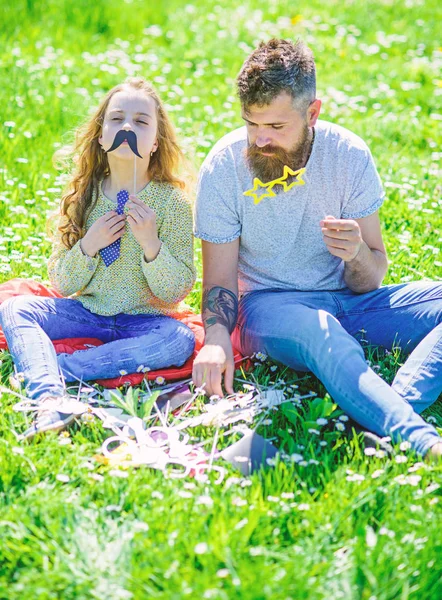 Baba ve kızı, grassplot, arka planı yeşil çimenlerin üzerinde oturur. Çocuk ve babası eyeglases ve muastache photo booth öznitelikleri ile poz. Aile zaman kavramı. Aile harcamak açık havada eğlence — Stok fotoğraf