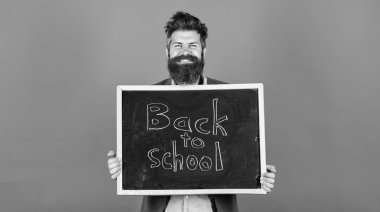 New semester in school. Teacher bearded man stands and holds blackboard with inscription back to school blue background. Teacher invites to continue studying. Continue your education with us clipart