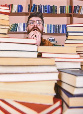 Kazık kitap kütüphane, kitap rafı arka plan üzerinde arasında gergin yüz kişi. Öğretmen ya da öğrenci sakallı gözlük takmaz, defocused kitaplar ile masada oturur. Bilimsel bir keşif kavramı