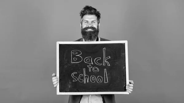 Új szemeszter az iskolában. Tanár szakállas ember áll, és tartja tábla felirattal vissza az iskola kék háttér. A tanár felkéri, hogy folytassa a tanulást. Folytasd velünk az oktatást. — Stock Fotó