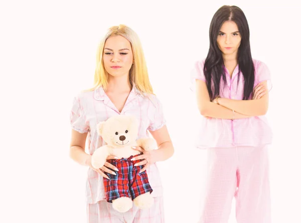 Sisters in pajamas looks unfriendly, jealous. Girls in pink pajamas, isolated white background. Jealousy and envy concept. Lady jealous to sister with plush toy bear, defocused — Stock Photo, Image