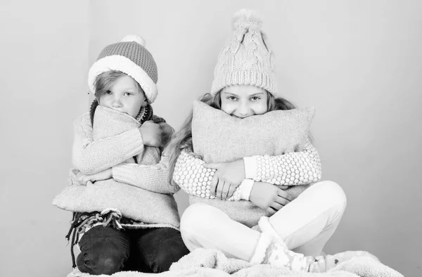 Warm up your winter wear with cute and cozy accessories. Siblings wear winter warm hats sit on pink background. Children boy and girl warm up with pillows and hats. Stay warm and comfortable