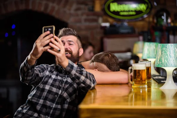 Hombre en el bar bebiendo cerveza. Tome una foto selfie para recordar la gran noche en el pub. Hombre barbudo hipster mantenga el teléfono inteligente. Tomando concepto de selfie. Comunicación en línea. Enviar selfie a amigos redes sociales —  Fotos de Stock