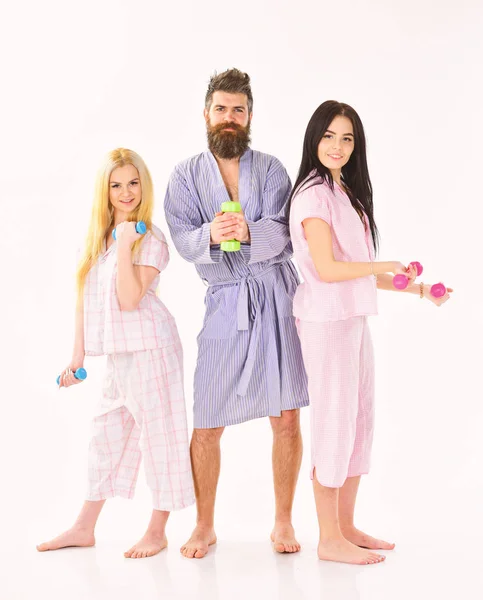 Bearded man with sporty ladies. Fitness morning concept. Company of friends with dumbbells in domestic clothes, isolated on white background. Trainer, macho with attractive girls do morning exercises