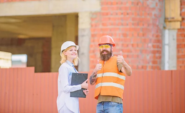 Discuss progress project. Woman inspector and bearded brutal builder discuss construction progress. Construction project inspecting. Safety inspector concept. Construction site safety inspection