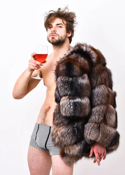 Chico atractivo rico posando abrigo de piel en cuerpo desnudo. Sexy soñoliento rico macho tousled pelo beber vino aislado en blanco. Salud y bienestar. Riqueza y concepto de lujo. Atleta rico disfrutar de su vida — Foto de Stock