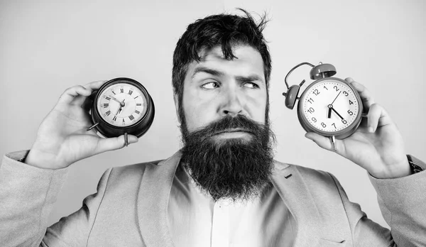 Man bearded hipster hold two different clocks. Guy unshaven puzzled face having problems with changing time. Changing time zones affect health. Time zone. Does changing clock mess with your health — Stock Photo, Image