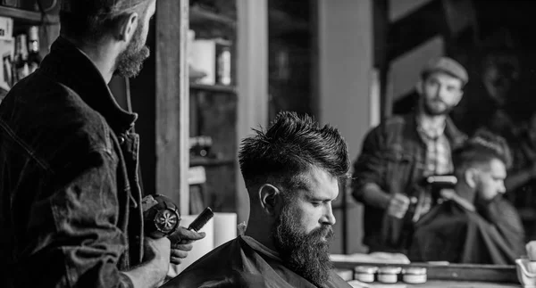 Hipster levensstijl concept. Kapper met föhn werkt op kapsel voor bebaarde man barbershop achtergrond. Hipster bebaarde client krijgen kapsel. Kapper met haardroger Droogrek voor client — Stockfoto