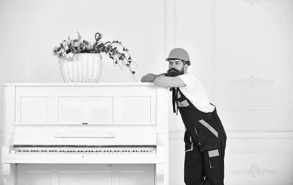 Nadenkende jongen leunend op de bovenkant van vintage witte piano met bloem glasvaas geïsoleerd op een witte achtergrond. Bebaarde werknemer genieten van korte pauze — Stockfoto