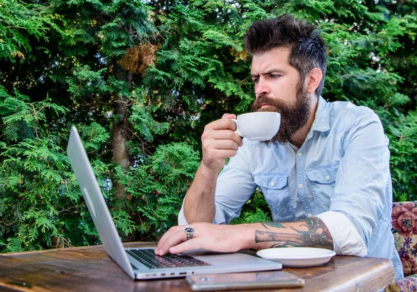 Equilibrio entre trabajo y placer. Hipster beber té y el uso de la computadora estación de trabajo al aire libre. Hombre barbudo haciendo su trabajo en línea. Trabajar globalmente a distancia —  Fotos de Stock