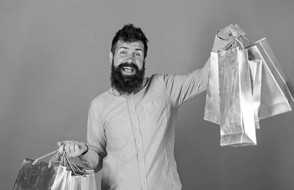 Man with big smile and beard holding silver paper bags, sales concept. Bearded man in pink shirt on red background. Hipster with cheerful face and trendy beard and mustache crazy about shopping — Stock Photo, Image