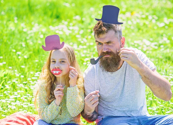 Dad and daughter sits on grass at grassplot, green background. Aristocrates concept. Child and father posing with top hat, lips and pipe photo booth attributes. Family spend leisure outdoors — Stock Photo, Image