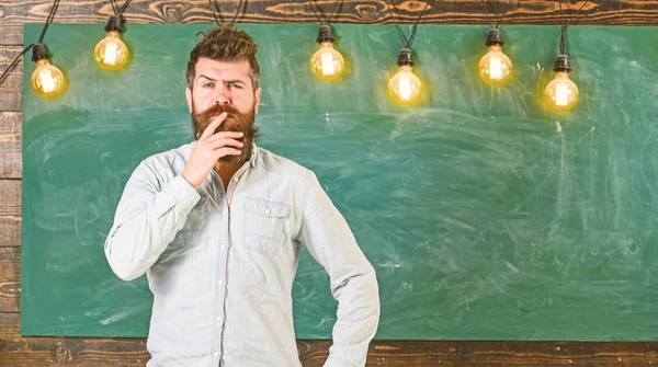 Intellectual task concept. Man with beard and mustache on thoughtful face stand in front of chalkboard. Bearded hipster in shirt, chalkboard on background. Guy thinking with thoughtful expression — Stock Photo, Image