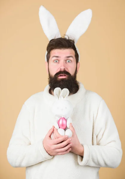 Ser parte de las vacaciones de Pascua. Celebración de las vacaciones de primavera. Conejo de Pascua entregando huevos de colores. Hipster con orejas de conejo sosteniendo la liebre ponedora. Hombre barbudo con juguete de conejo y huevo de Pascua — Foto de Stock