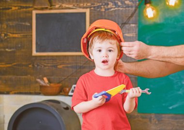Oyuncak araçları ile oynayan heyecanlı çocuk. Sarışın çocuk atölyede bağırarak. Baba küçük yardımcısı. Turuncu koruyucu kask tutan erkek el