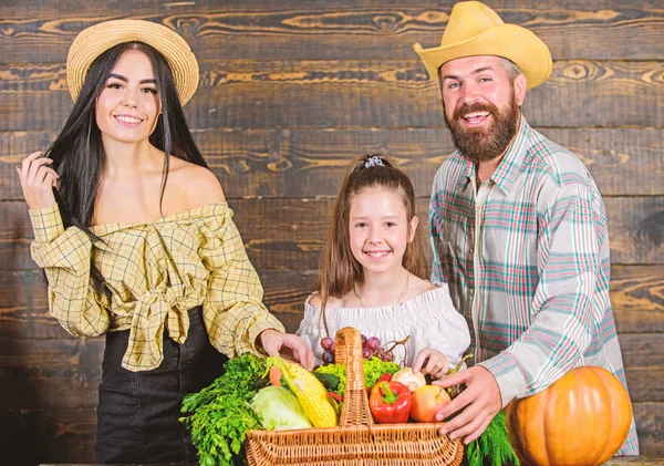 Family farmers with harvest wooden background. Family rustic style farmers market with fall harvest. Parents and daughter celebrate harvest holiday pumpkin vegetables basket. Harvest festival concept