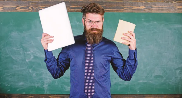 Digital contra papel. Professor hipster barbudo detém livro e laptop. O que prefere? Professor escolhendo abordagem de ensino moderno. Escolha o método correto de ensino. Livro de papel contra laptop — Fotografia de Stock