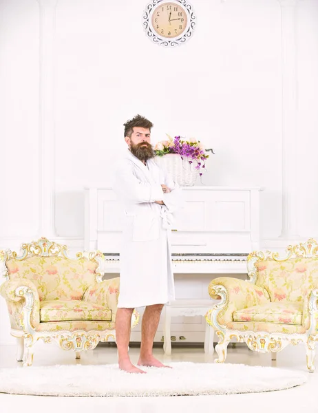 Full length portrait of a young man in a robe isolated in white room. Brutal bearded guy standing with his arms crossed at his chest. Morning in rich mans house