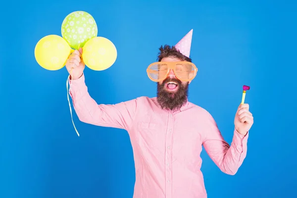 Чоловік з бородою і вусами на щасливому обличчі тримає повітряні кульки, синій фон. Хіпстер у гігантських окулярах, що святкують день народження. Хлопець у вечірньому капелюсі з святковими атрибутами святкує. Концепція партії — стокове фото