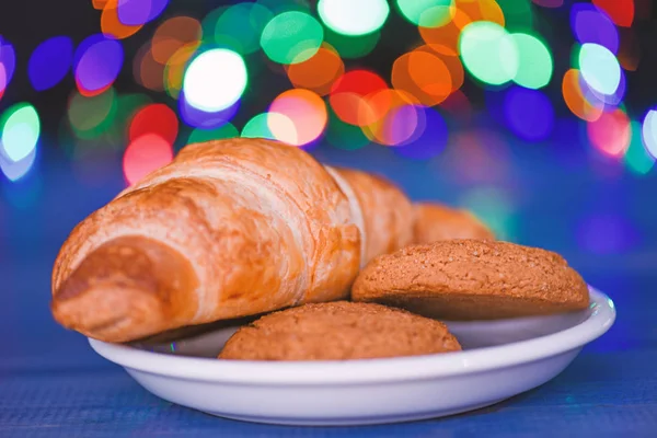 Croissant and oat cookies on white plate. Winter holiday tradition. Sweets for Santa Claus and his helpers. Santa treats recipe. Treats for Santa concept. What do kids around world leave for Santa