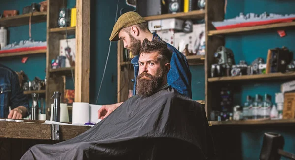 Hipster client getting haircut. Client with beard ready for trimming or grooming. Haircut process concept. Man with beard covered with black cape waiting while barber changing clipper grade