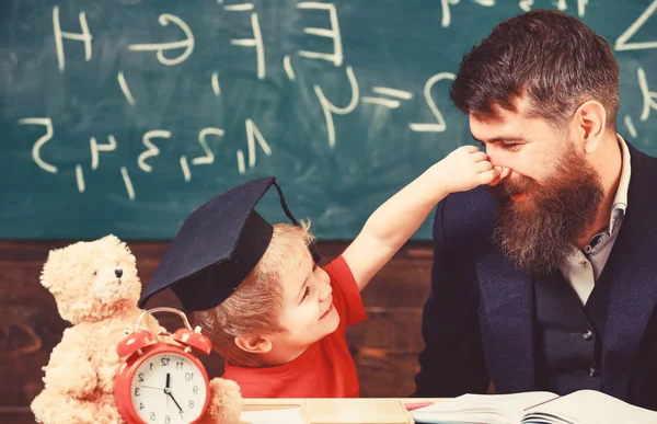 Játékos gyermek koncepció. Vidám gyerek játék, apa. Szakáll, apa, tanár tanítja fiát, kisfiú, míg a gyermek csipkedte az orrát. Tanár és a tanuló mortarboard, háttér chalkboard — Stock Fotó