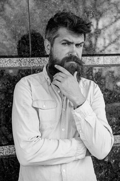 Man with beard and mustache on thoughtful, pensive face, black marble background. Masculinity concept. Hipster with tousled hair touches beard while looking into distance. Guy looks suspicious — Stock Photo, Image