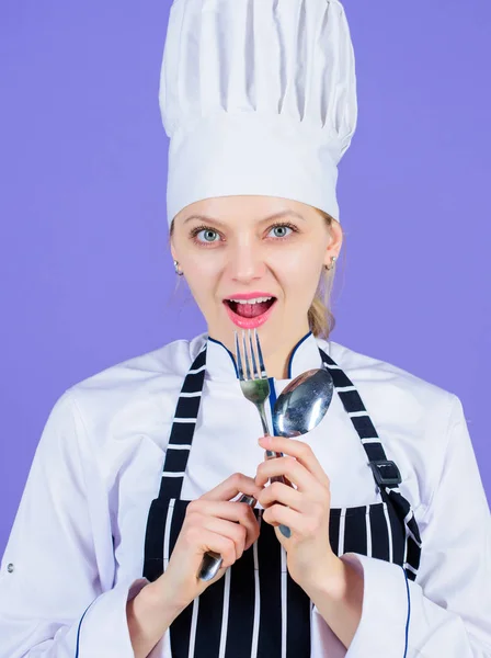 Είμαι πολύ καλή μαγείρισσα. Αισθησιακή μαγείρισσα. Όμορφη μαγείρισσα κρατώντας ανοξείδωτο χάλυβα κουτάλι και πιρούνι. Επαγγελματική μαγείρισσα φορώντας παραδοσιακό λευκό καπέλο σεφ και ποδιά — Φωτογραφία Αρχείου
