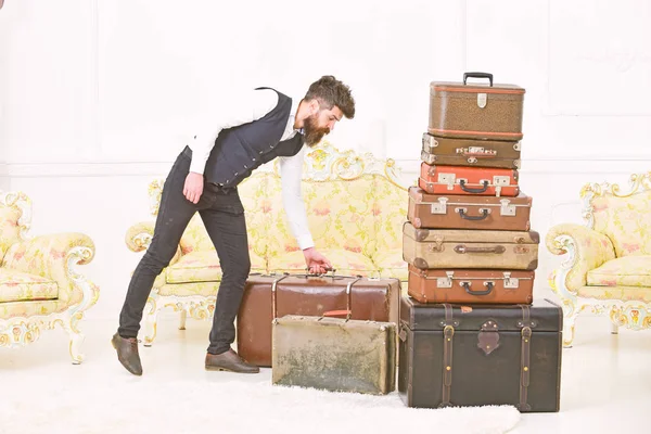 Macho elegant on strict face carries vintage suitcase. Man, butler with beard and mustache wearing classic suit delivers luggage, luxury white interior background. Luggage and relocation concept