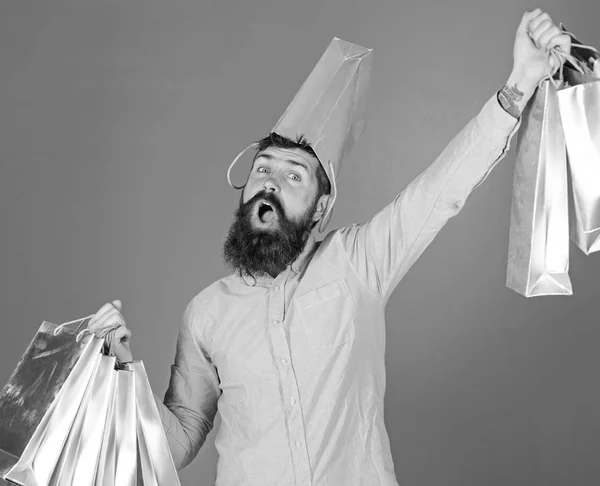 Guy shopping on sales season with discounts. Man with beard and mustache carries shopping bags, blue background. Hipster on happy face with bag on head is addicted shopaholic. Shopping concept — Stock Photo, Image