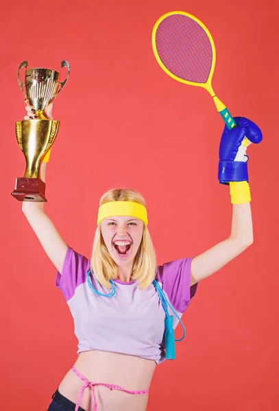 Sport equipment store. Sport shop assortment. Girl cheerful successful modern woman hold golden goblet of sport champion and equipment red background. Sport for every day. How to stay fit forever