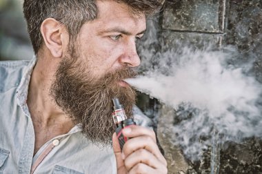 Sakallı adam vape, beyaz bulutlar duman sigara içiyor. Elektronik sigara kavramı. Uzun sakallı adam rahat görünüyor. Adam sakal ve bıyık sakin yüz, koyu arka plan, defocused