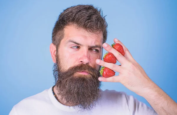 Hipster skägg mustasch vackert ansikte tycker bär. Mannen skäggig hipster hålla hand med jordgubbar nära ansiktet. Jordgubbe på mitt sinne. Man kan inte tänka på något annat än jordgubbe blå bakgrund — Stockfoto