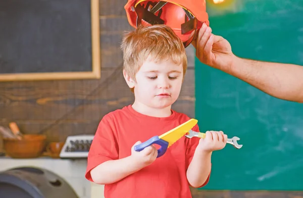 Skoncentrowany dziecko patrząc na narzędzia w jego ręce. Chłopiec uczenia się nowych umiejętności. Tatuś, zdejmując kask z synem — Zdjęcie stockowe