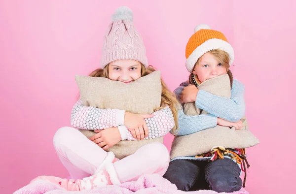 Wärmen Sie Ihre Winterbekleidung mit netten und gemütlichen Accessoires auf. Geschwister tragen winterwarme Hüte auf rosa Hintergrund. Kinder wärmen sich mit Kissen und Hüten auf. Bleiben Sie warm und bequem — Stockfoto