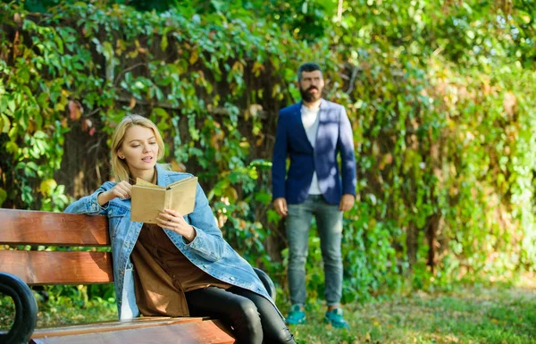 Kobieta przeczytać ciekawą książkę, siedząc na ławce w parku. ciekawe książki. Mężczyznę idącego w parku. Forst spotykają się na pary. W weekend wiosna lato. Czas na relaks i romantyczny czytania. Ciekawa historia czytania — Zdjęcie stockowe