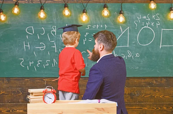 Leerling in afstuderen GLB op te lossen vergelijking met de hulp van de leraar. Man kleine jongen rekenkundig onderwijs terwijl wijzend op het bord met getallen. Volwassen man en een jongen keerde terug in de klas — Stockfoto