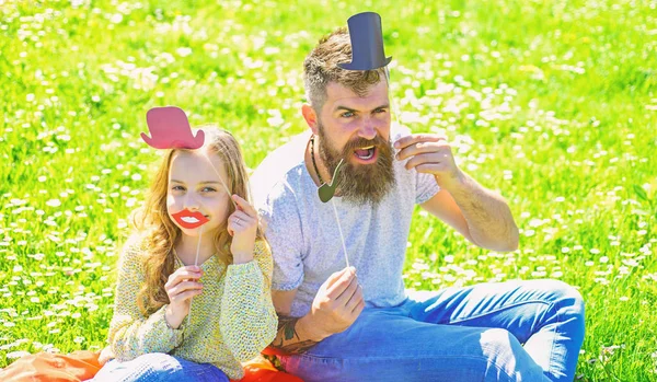 Conceito Aristocrates. O pai e a filha sentam-se na relva no campo, fundo verde. Família passar o lazer ao ar livre. Criança e pai posando com chapéu superior, lábios e atributos de cabine de fotos de tubulação — Fotografia de Stock