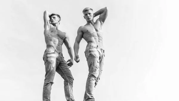 Sexy torso attractive body. Denim pants emphasize masculinity sexuality. Men twins brothers muscular guys posing with muscles sky background. Men strong muscular athlete bodybuilder. Divine beauty